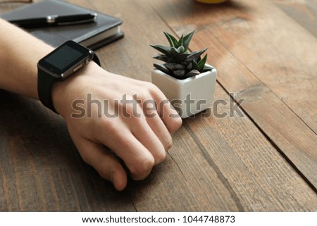 A man's hand with a smart watch and a small decorative cactus on a wooden background.