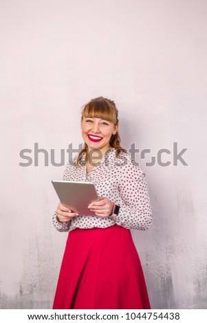 young beautiful girl in a red dress stands on a pink background and holds a tablet