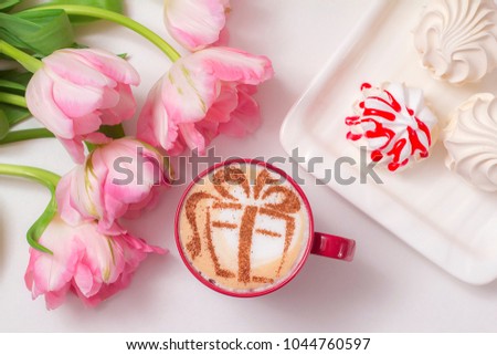 cappuccino in a red mug with a picture of a gift on milk foam surrounded by flowers of tulips and sweet marshmallows