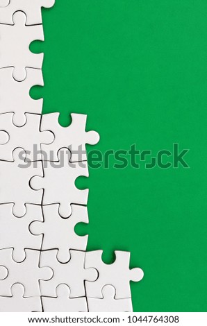 Fragment of a folded white jigsaw puzzle on the background of a green plastic surface. Texture photo with copy space for text
