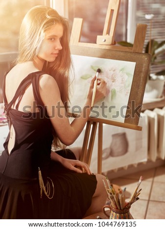 Artist painting on easel and palette in studio. Authentic girl paints with oil brush morning sunlight dawn light toning window background. Quiet environment for creativity. Sun flare drawing homework