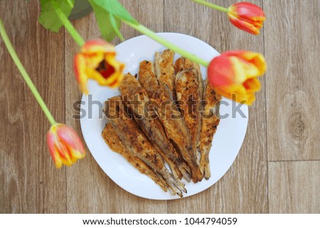 Grilled fish on a white plate on the wooden background and beautiful blurred tulips