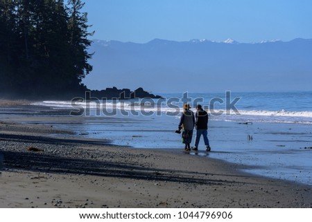 A couple walking along French Beach Provincial Park with the views of the Strait of Juan de Fuca and the Olympic Mountains, British Columbia, Canada