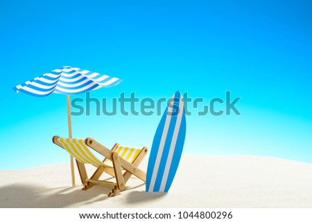 Deck chair under an umbrella and a surfboard on sandy beach, sky with copy space