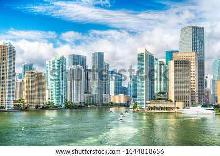 Aerial view of Miami skyscrapers with blue cloudy sky, white boat sailing next to Miami downtown. miami luxury property, modern buildings and yachts
