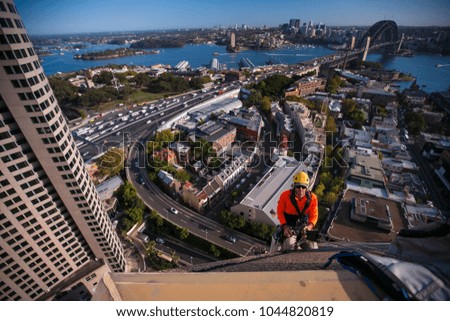 Aerial view of rope access worker wearing safety yellow hard hat, long sleeve shirt harness, and a white bucket, working, descending from high rise building at circular quay, Sydney, Australia