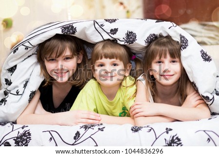 Funny little sisters hides under a blanket. Cute girls having fun on the bed. Concept of kids sleep, care or childhood