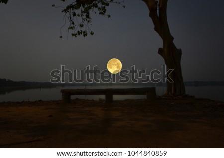 Lonely wooden seat with beautiful full moon over the lake