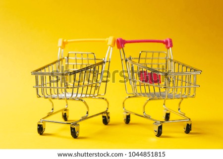 Close up of two supermarket grocery push carts for shopping with wheels and yellow and pink plastic elements on handle isolated on yellow background. Concept of shopping. Copy space for advertisement.