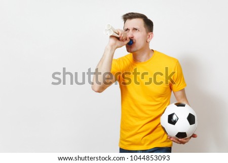 Inspired young fun cheerful European man, fan or player in yellow uniform hold soccer ball, pipe, cheer favorite football team isolated on white background. Sport, play football, lifestyle concept
