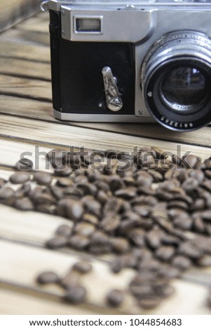 The old camera next to the coffee beans scattered from the bag, on a wooden background.