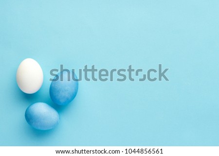 Blue painted eggs with white natural egg on blue baackground, monochrome top-view 