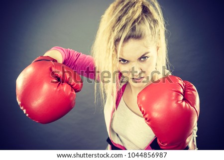 Sporty angry determined woman wearing red boxing gloves, fighting. Studio shot on dark background.