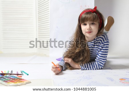 Cute  girl draws on the big sheet of paper lying on a floor