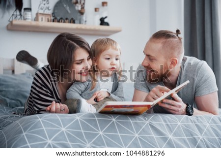 Parents and Little Daughter Reading Children's Book on a Sofa in the Living Room. Happy family read an interesting book on a festive day. 