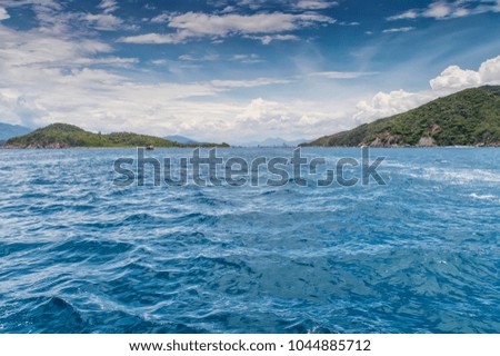 islands in the sea, covered by dense equatorial greenery, a motor boat in the background walking along the sea, a city on the horizon, against the backdrop of mountains and sky covered with clouds