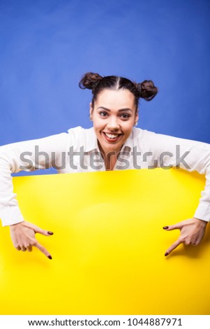 Woman next to a yellow board poster over blue background in studio photo