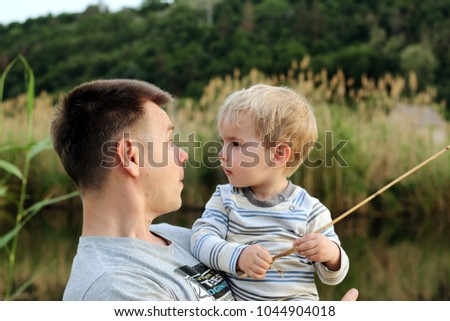 Portrait of a pretty little 3-year old boy with his father having fun and a rest on the bank of the pond in the forest, sunny day, happy family weekend, early spring outdoor