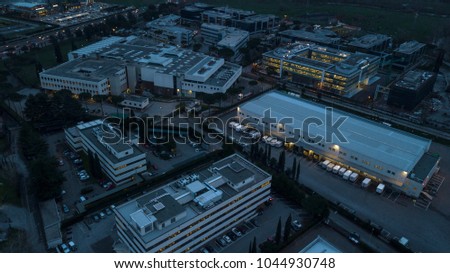 Aerial night view of an industrial area of a large Italian city with warehouses, offices and buildings. Among the asphalt roads beyond the cars, vans and trucks there are trees. Royalty-Free Stock Photo #1044930748