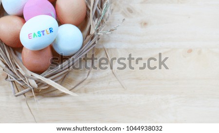 Many white, pink and orange eggs are in the basket and puts on the vintage wooden table. Easter wording is on the white egg. The picture concepts for celebration, coming again with copy space.