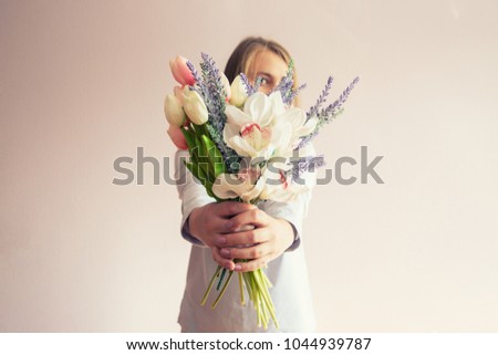 A young beautiful girl with blond dissolved long hair, a felt hat on her head, keeps spring flowers in her hands on a sunny day. Women's Day.
