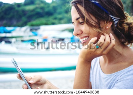 Pretty woman near the ocean, smiling and using mobile phone