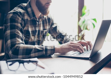 Cropped close up photo of serious concentrated handsome confident busy red bearded guy, hands fingers typing email on laptop sitting at the table in office near window
