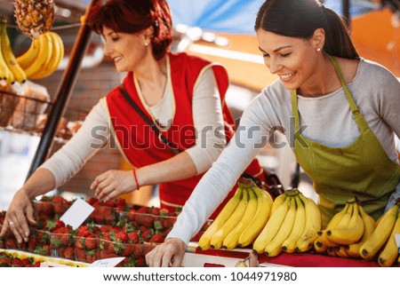Two saleswoman on fruit market selecting fresh fruit and preparing for working day.