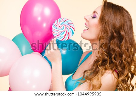 Woman attractive cheerful girl holding colorful balloons and sweet lollipop in hands. Summer holidays, celebration and happiness concept. Studio shot bright yellow background