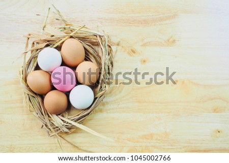 Many pink, white and orange eggs are in the straw basket and put it on the wooden table. The picture concepts for Easter, natural, painting, organic, fresh, food, healthy with copy space.