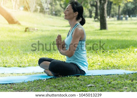Middle-aged Caucasian woman doing Yoga in the parks. Young girl setting on Yoga mat on the grass in the park exercises outdoors.healthy lifestyle concept.