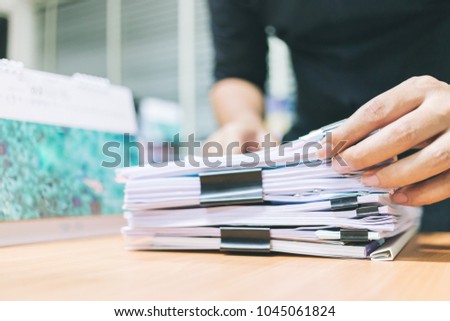 Hand of businessman for searching information in Stacks of paper on work desk office.