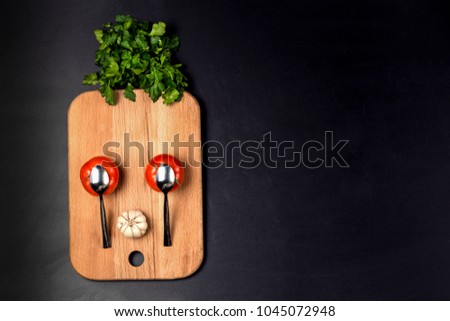 cartoon funny surprised face of tomatoes, spoons, garlic and parsley lined on the kitchen wooden board, with space for text, the concept of creative and fun cooking, flat lay image