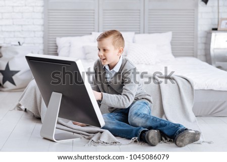 Pleasant entertainment. Delighted happy positive child smiling and sitting in front of the screen while being at home