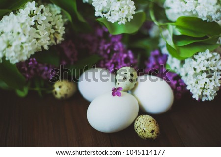 Chicken and quail eggs in a bouquet of lilac on a wooden table