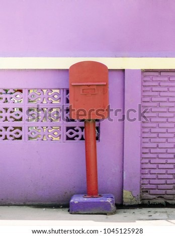 Red colour post box of Uthaithani province,  Thailand with purple - violet concrete wall