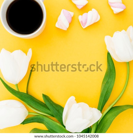 Frame made of white tulips flowers with mug of coffee and marshmallows on yellow background. Floral concept. Flat lay, top view.
