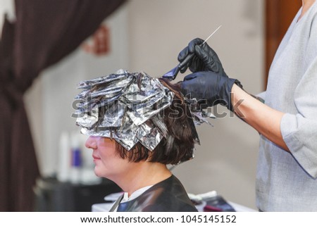 hairdresser coloring client woman hair in beauty barber studio salon, using brush and foil, professional dye and treatment concept