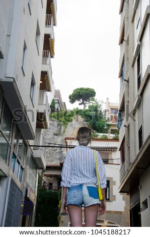 Young woman in a white shirt and with a yellow little bag tourist walking on the streent of Lloret de Mar in a beautiful summer day, Costa Brava, Catalonia, Spain. Streets of Europe.