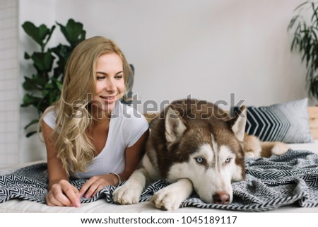 Authentic portrait of happy smiling female and husky in perfect apartment for living. Cute curly hair woman and adorable dog posing for pictures at cozy home.