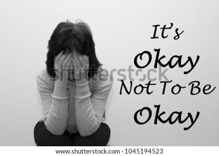 Woman with her head in her hands with the saying It's okay not to be okay written on the wall.
