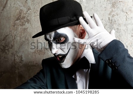Scary evil clown wearing a bowler hat on wall background