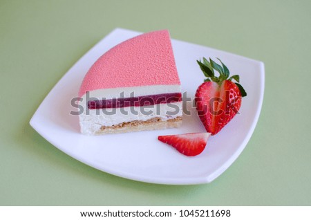 Slice of strawberry cake with white chocolate mousse decorated with fresh strawberry on white plate on green background