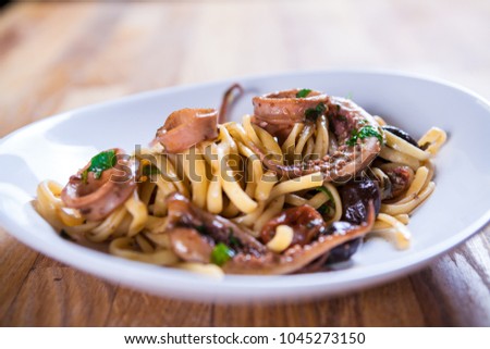 Pasta with calamari seasoned with red cherry olives and basil. Calamari spaghetti on white plate. Mediterranean pasta. seafood. Italian food. Fine dish