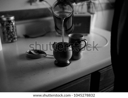 A black and white photo of a man pouring a french press coffee into coffee mugs.
