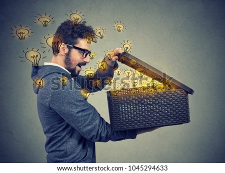 Happy surprised man opening a box with many bright light bulbs flying out Royalty-Free Stock Photo #1045294633