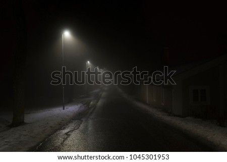 Foggy night in Sweden Scandinavia Europe. Beautiful, mystical and abstract photo of dark winter evening with mist in air. Calm, peaceful outdoors image with lights, lamps and road.