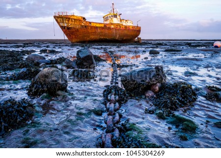 Rusty old fishing vessel marooned at low tide on a mud bank the boats long big anchor chain goes from the centre foreground to the boat in the background