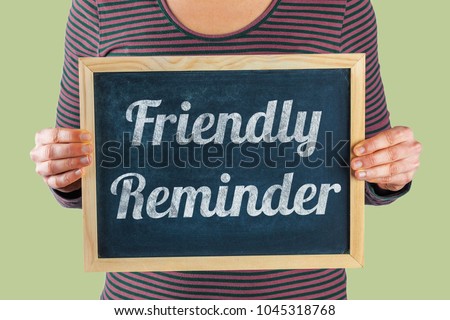Female hands holding small black chalkboard in front of the body with written words saying Friendly Reminder Royalty-Free Stock Photo #1045318768