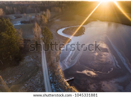 Aerial Drone Photograph of a Partly Frozen Lake Surrounded with Beautiful Winter Colors of the Fields and Forest - Sun Flare